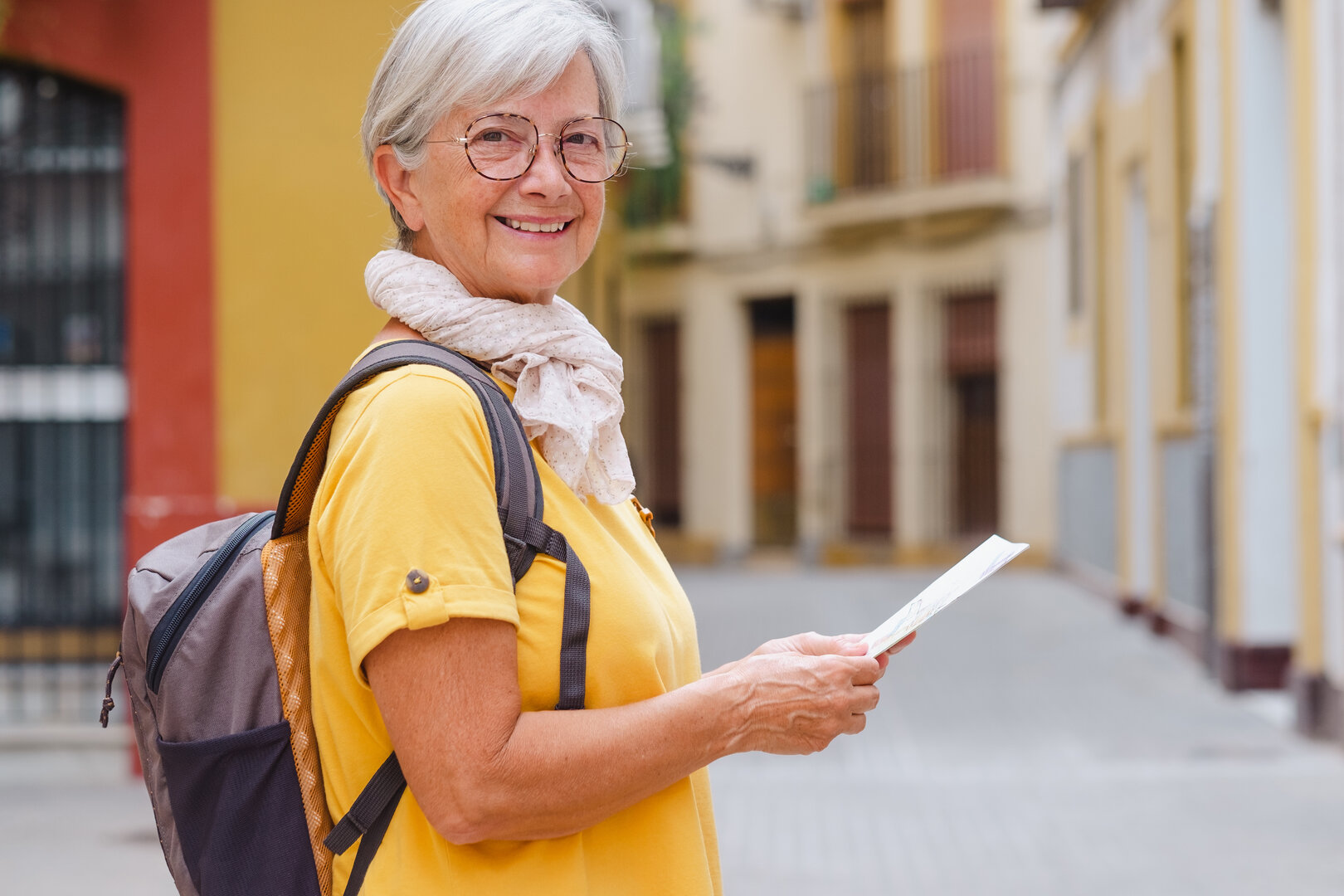 mujer mayor sonriendo mientras sostiene un mapa en una calle soleada de España