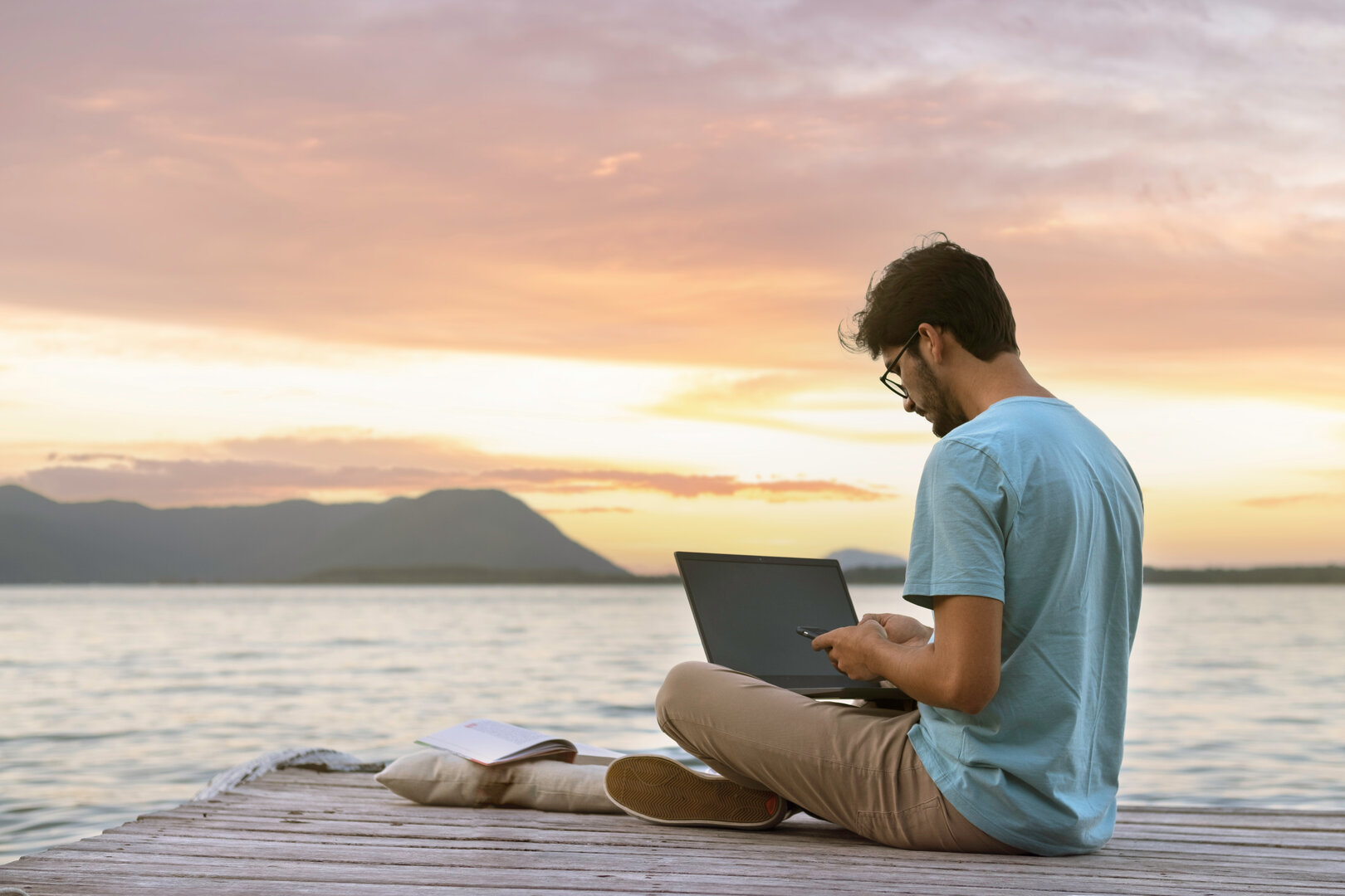 hombre sentado junto al mar utilizando un ordenador portátil al atardecer